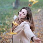Young woman with arms outstretched, delighting in fallen leaves in a Paris park during autumn daytime.